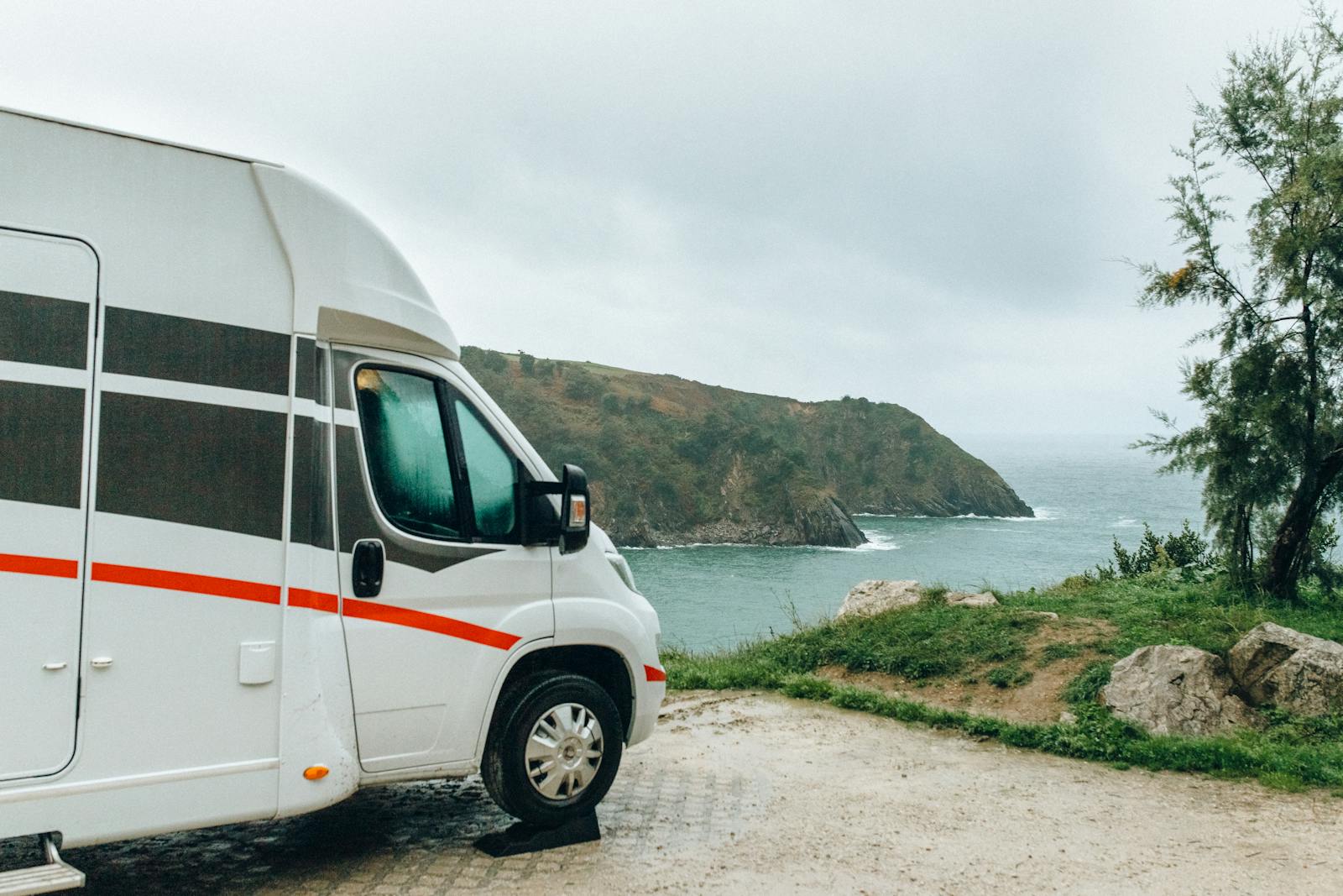 Scenic view of a camper van parked by the ocean cliffs on a cloudy day.